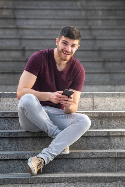 Dışarıda merdivenlerde cep telefonuyla oturan genç adamın portresi.