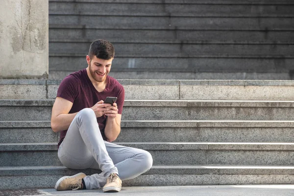 Helkroppsporträtt Stilig Ung Man Som Sitter Trappan Och Tittar Mobilen — Stockfoto