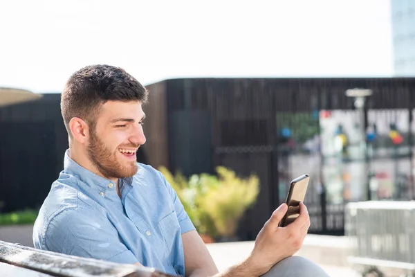 Портрет Счастливого Молодого Человека Сидящего Снаружи Смотрящего Мобильный Телефон — стоковое фото