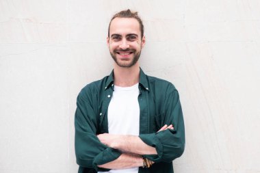 Beyaz arka planda kolları ve sakalı çaprazlanmış gülümseyen genç adamın portresi.