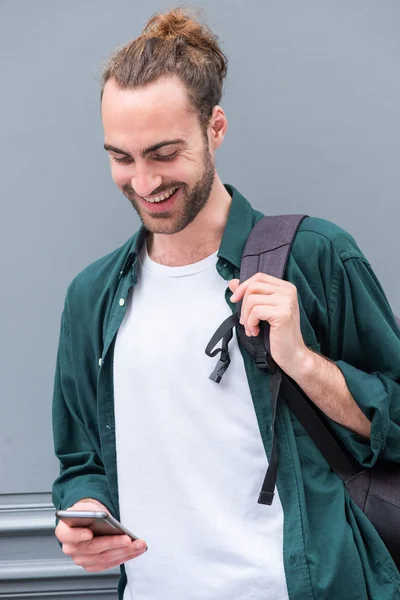 幸せな若い男の肖像画笑顔で携帯電話とバッグによってグレーの壁 — ストック写真