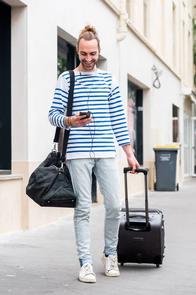 Full body portrait of travel man with luggage and mobile phone walking in city