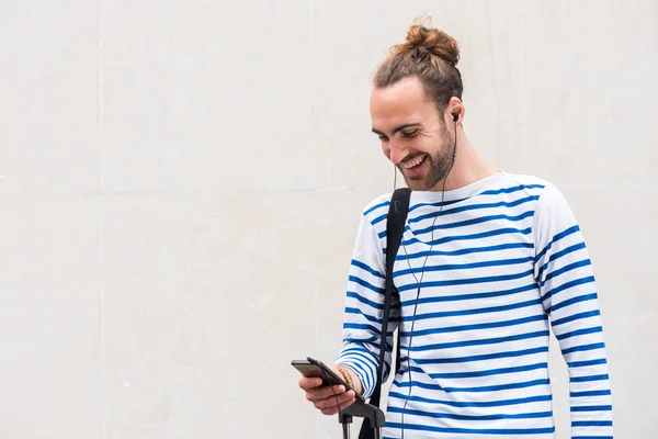 白い背景でイヤホンで音楽を聴きながら携帯電話を見て幸せな若い男の肖像画 — ストック写真