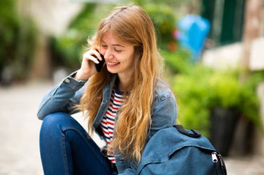 Dışarıda oturmuş cep telefonuyla konuşan mutlu genç bir kadının portresi.