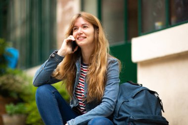 Dışarıda oturmuş telefonla konuşan genç bir kadın portresi.