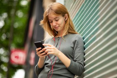 Kulaklık ve cep telefonuyla müzik dinleyen genç bir kadının portresini kapat.