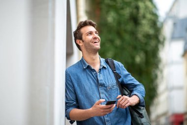 Duvara yaslanmış cep telefonu tutan mutlu bir portre.