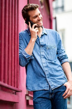 Dışarıda duvara yaslanmış, cep telefonuyla konuşan yakışıklı bir adamın portresi.
