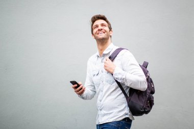 Gri arka planda çantalı ve cep telefonlu yakışıklı yaşlı bir adamın yan portresi.