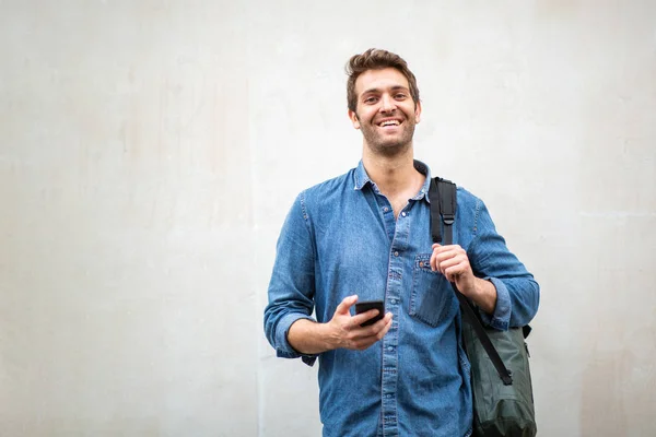 Portrait smiling man with mobile phone and bag by white wall