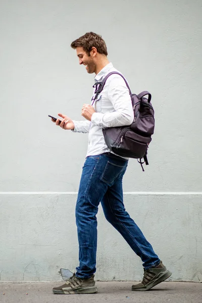 フル体ポルノの幸せな旅行男とともにバッグ見ますの携帯電話によってグレーの壁 — ストック写真