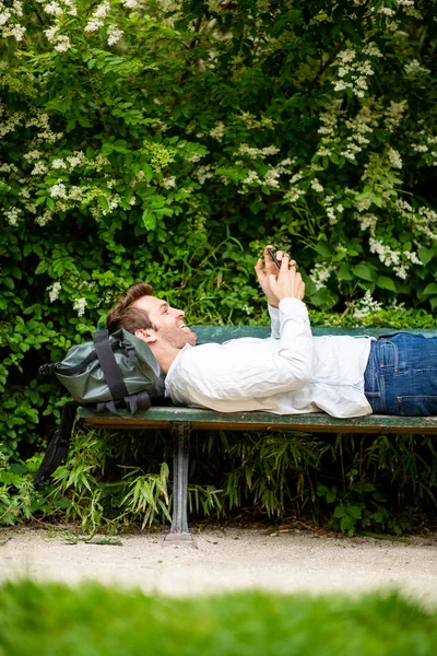 Портрет Счастливого Человека Лежащего Скамейке Парке Мобильным Телефоном — стоковое фото