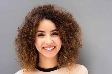 Gri arka planda gülümseyen kıvırcık saçlı güzel bir genç kadının ön portresini kapat.