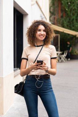 Şehirde cep telefonu ve kulaklığı olan gülümseyen Afro-Amerikan kadının portresi.