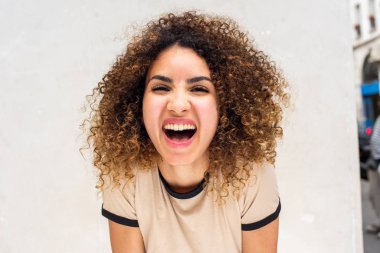 Beyaz duvarlara karşı gülen kıvırcık saçlı Afro-Amerikan kadının yakın portresi.