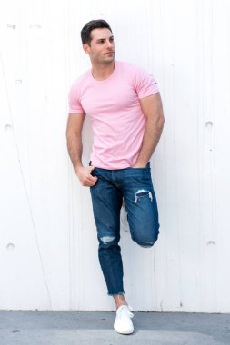 Beyaz duvara yaslanmış havalı bir gencin tam boy portresi.