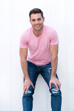 Beyaz arka planda elleri dizlerinde gülümseyen yakışıklı genç adamın portresi. 