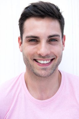 Beyaz duvarda gülümseyen yakışıklı bir gencin yakın portresi.