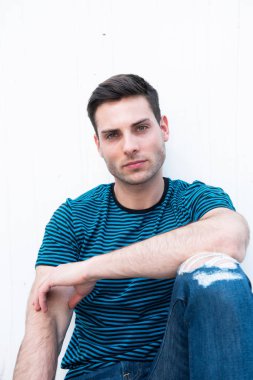 Beyaz duvarda oturan yakışıklı genç adam. 