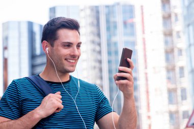 Şehirde cep telefonu ve kulaklıkla gülümseyen genç adamın portresi