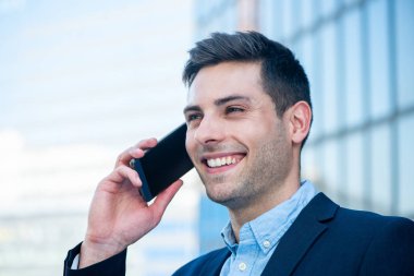 Şehirde cep telefonuyla konuşan gülümseyen iş adamının yan portresini kapat.