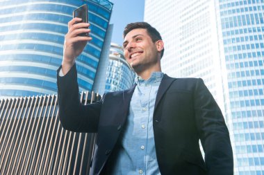 Şehirde cep telefonuna bakan gülümseyen genç iş adamı portresi