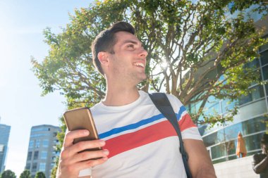 Dışarıda cep telefonu ve çantasıyla duran mutlu adamın portresini kapat.