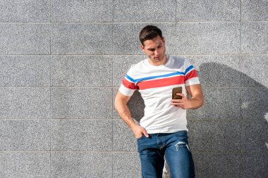 Gri duvarda cep telefonuna bakan yakışıklı bir gencin portresi.