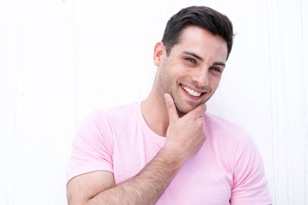 Close up portrait of handsome young man smiling by white background with hand on chin 