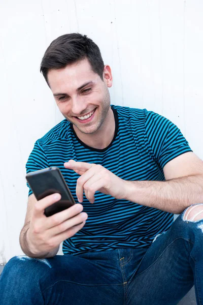 Retrato Jovem Feliz Sentado Parede Branca Olhando Para Telefone Móvel — Fotografia de Stock