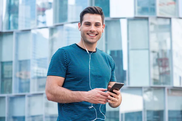 肖像画笑顔の若い男は 市内の外にイヤホンで携帯電話を保持 — ストック写真