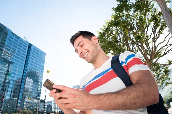 街で携帯電話やバッグと笑顔の若い男のサイドポートレート — ストック写真