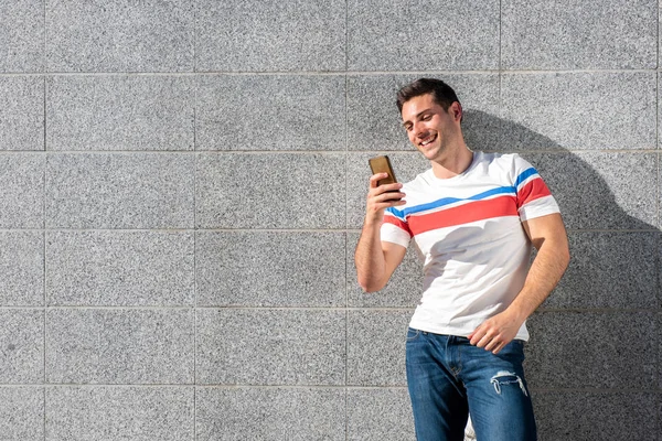 Retrato Del Joven Sonriendo Mientras Mira Teléfono Móvil Por Pared — Foto de Stock