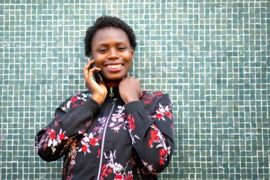 Close up front portrait happy african woman leaning against wall talking with cellphone