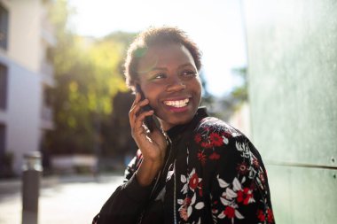 Close up portrait happy young african woman talking with cellphone outside