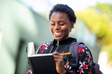 Close up portrait smiling young african woman walking outdoor with book
