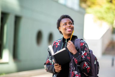 Close up portrait smiling young african woman walking in city with book