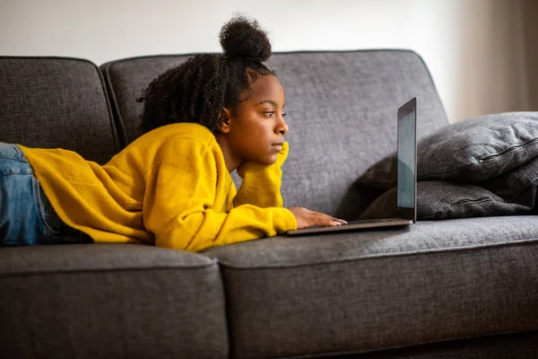 ポートレートアフリカの女の子うそ上のソファ見ますのラップトップコンピュータ画面にホーム — ストック写真