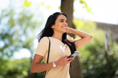 Side portrait beautiful young smiling woman holding mobile phone outside 