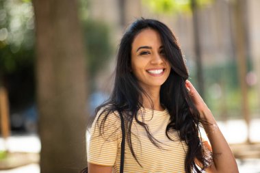 Close up portrait of happy young arabic woman smiling with hand in hair outside