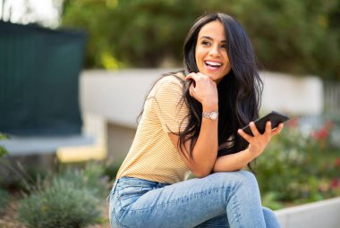 Portrait young woman sitting outside holding cellphone and smiling