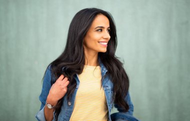 Close up portrait smiling young latin woman looking away by green wall