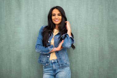 Portrait smiling young latin woman leaning against green wall 