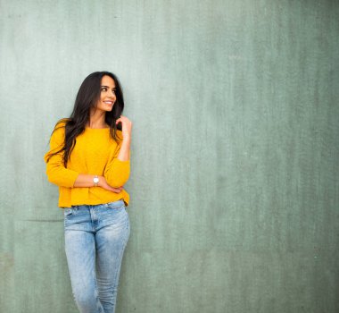 Çekici genç Latin kadın yeşil duvarda poz veriyor ve başka tarafa bakıyor.