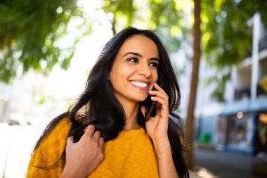 Kapalı portre, gülümseyen genç İspanyol kadın şehirde cep telefonuyla yürüyor ve konuşuyor.