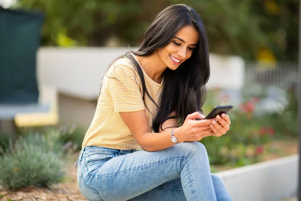 Retrato Sorrindo Jovem Mulher Sentada Fora Olhando Para Telefone — Fotografia de Stock