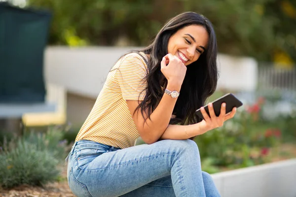 Retrato Mujer Joven Sentada Afuera Mirando Teléfono Celular Riendo — Foto de Stock