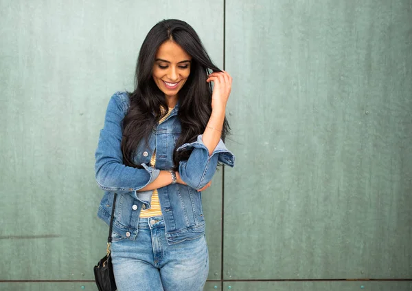 Portrait young arab woman with purse smiling with hand in hair by green wall