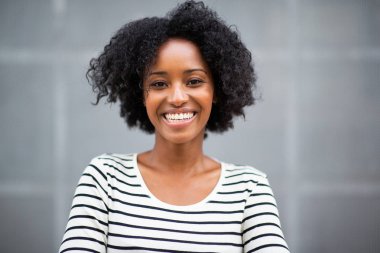 Gri duvarda gülümseyen güzel Afro-Amerikan kadın portresini yakından çek.