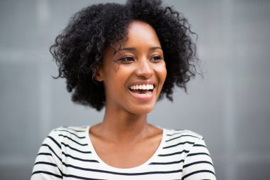 Gri duvarda gülümseyen ve yüzünü çeviren güzel Afro-Amerikan kadın.